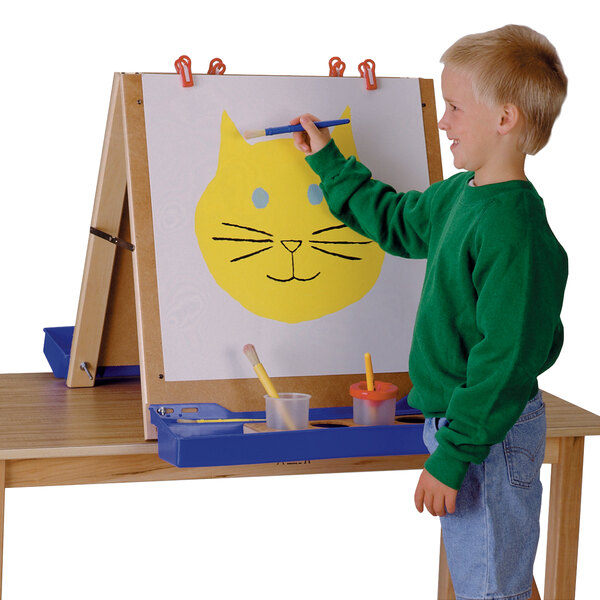 A young boy painting a cat on a Jonti-Craft Double Tabletop Easel.