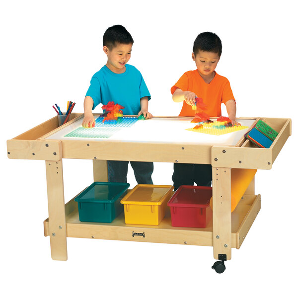 Two children playing with a Jonti-Craft light station on a large table with colored paper.