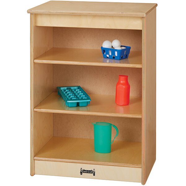 A Jonti-Craft toddler kitchen refrigerator with a blue tray with holes and a green plastic pitcher on a wooden shelf.