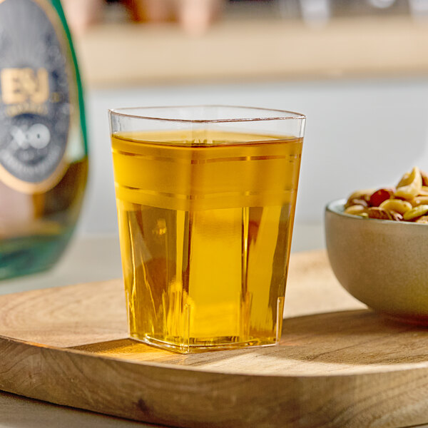 A clear Fineline Tiny Tumbler filled with yellow liquid on a wooden surface.