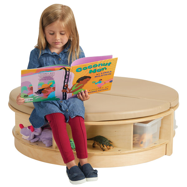A girl reading a book on a Jonti-Craft Read-a-Round island with padded seats.