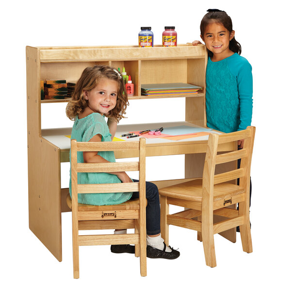 Two girls sitting at a Jonti-Craft wooden dual writing desk with an overhead shelf.