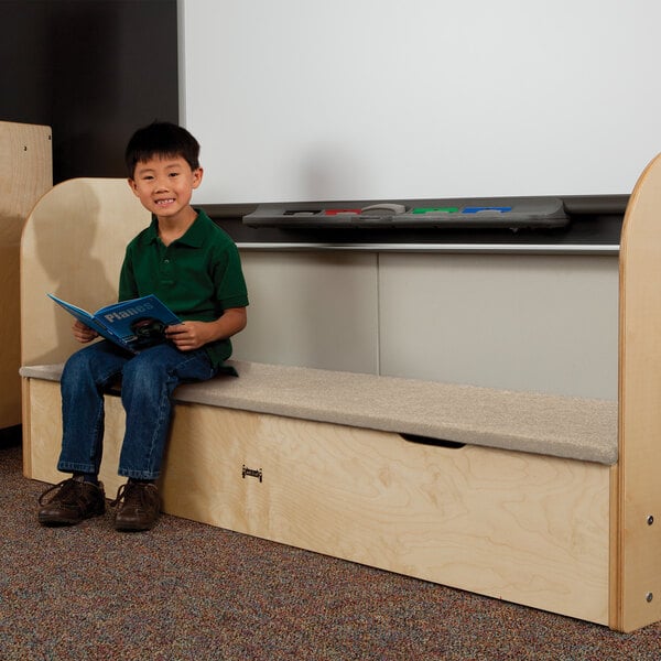 A boy reading a blue book while sitting on a Jonti-Craft storage step.