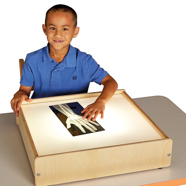 A young boy sitting at a table with a Jonti-Craft wood frame LED light box.