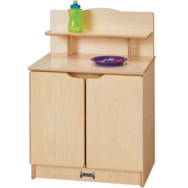 A Jonti-Craft wooden toddler kitchen cupboard with a blue plate and green bowl inside.