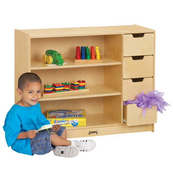 A young boy sitting on the floor next to a Jonti-Craft wood storage module with yellow drawers.