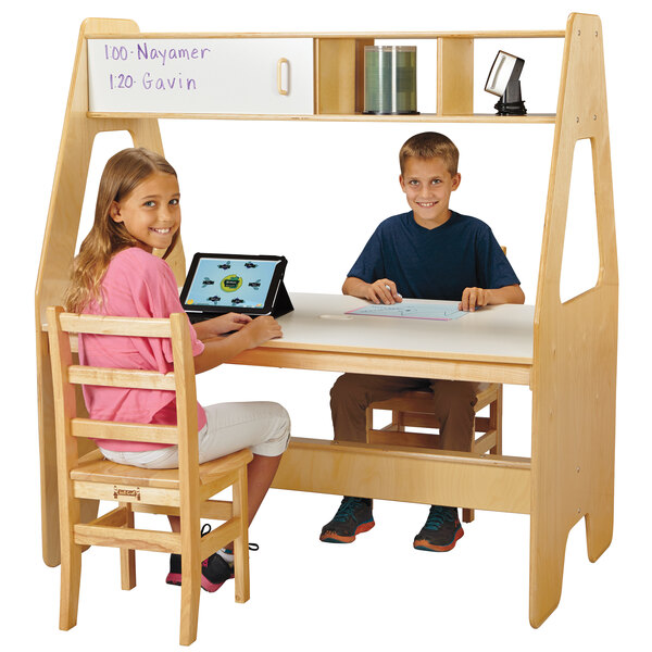A boy and girl sitting at a Jonti-Craft Children's Wood Workspace Center using a tablet.