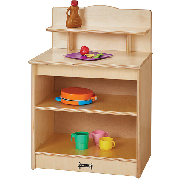 A Jonti-Craft toddler kitchen cupboard with a wooden shelf holding a green cup and a pink and yellow mug.