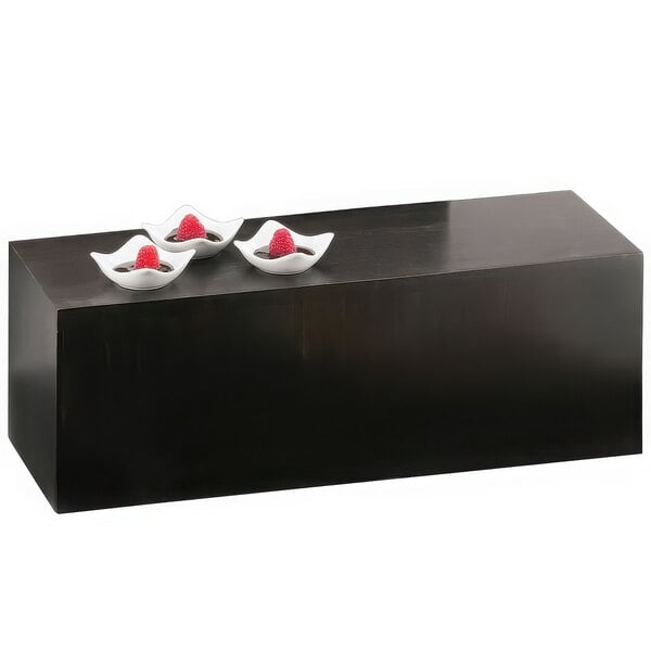 A black rectangular Cal-Mil plate riser with white bowls of red berries on it.