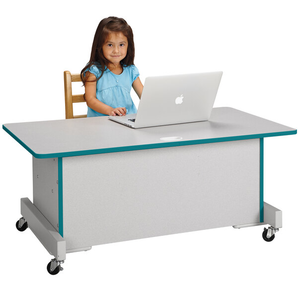 A young girl sitting at a Rainbow Accents computer desk using a laptop.