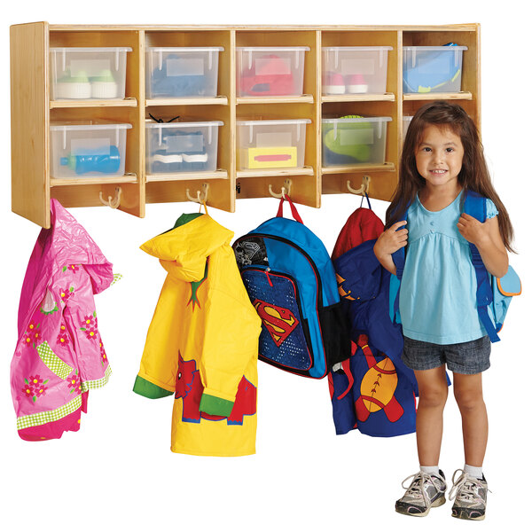 A little girl standing next to a Jonti-Craft wall mount coat locker with clear trays.