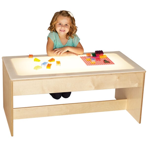 A girl sitting at a Jonti-Craft wood table with a lighted top.