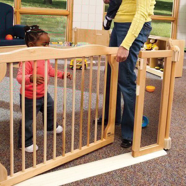 A woman standing behind a KYDZ Suite Welcome Gate with a child in a pink shirt and jeans.