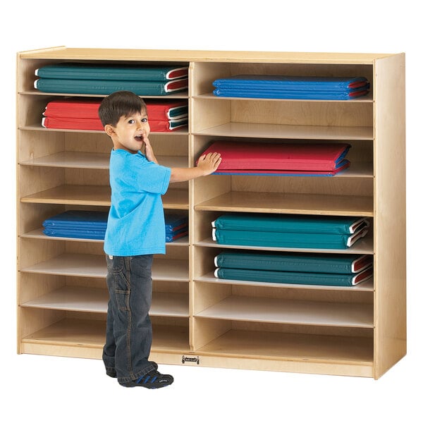 A boy in a blue shirt standing next to a Jonti-Craft wood mat storage cabinet.