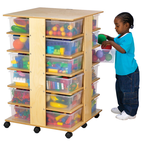 A child standing next to a Jonti-Craft mobile wood tub storage tower filled with plastic containers of toys.