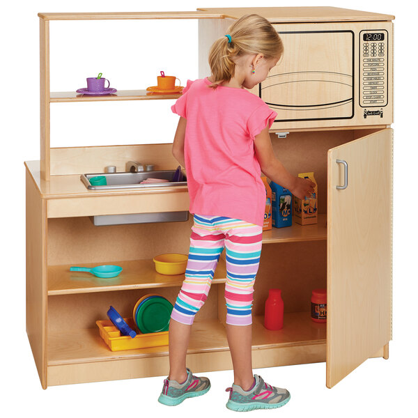 A girl playing with a Jonti-Craft wooden mobile kitchen island with sink, stove, microwave, and refrigerator.