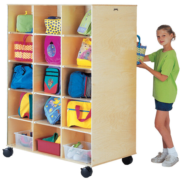 A girl putting a blue bag into a Jonti-Craft wood storage unit.