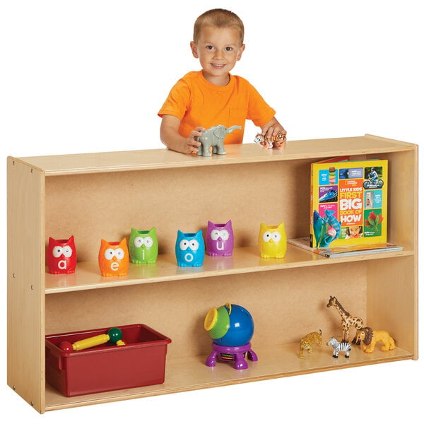 A young boy standing behind a Young Time natural wood storage shelf with toys.