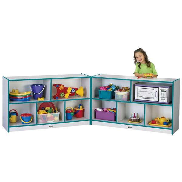 A little girl standing in front of a Rainbow Accents teal and gray storage cabinet with toys inside.