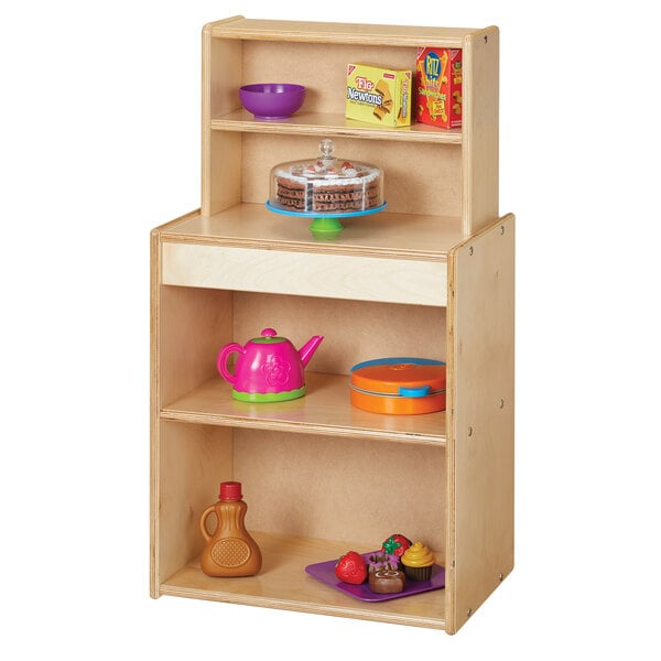 A Young Time natural wood play kitchen cupboard with shelves and food on it.