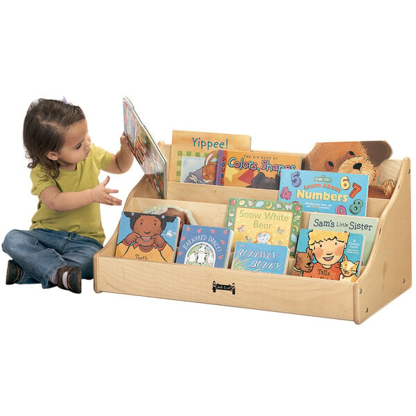 A child sitting next to a Jonti-Craft wood book rack full of books.