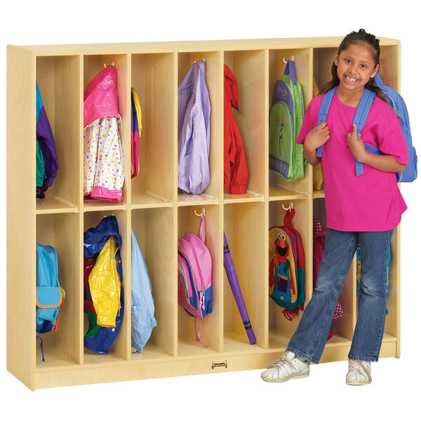 A young girl in a pink shirt standing in front of a Jonti-Craft locker with her backpack inside.