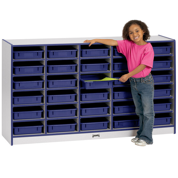A young girl standing next to a Rainbow Accents blue communication center with blue paper trays on a shelf.