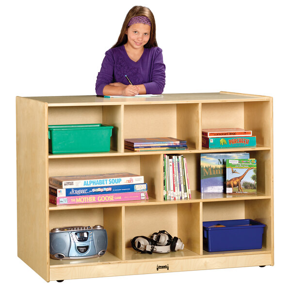 A girl standing behind a double-sided wood storage island with books on it.