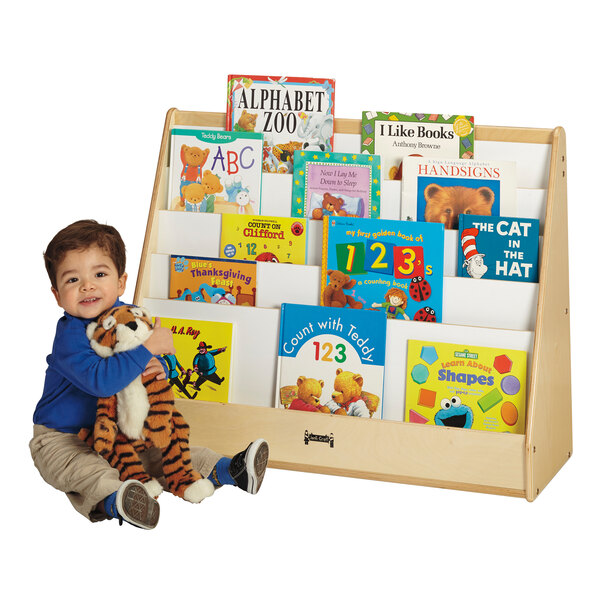 A child holding a stuffed tiger next to a Jonti-Craft wood book rack.