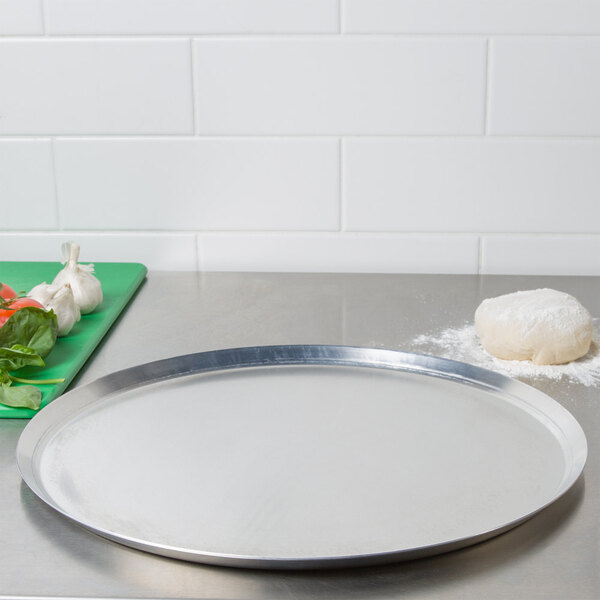 An American Metalcraft 18" heavy weight aluminum pizza pan on a counter.