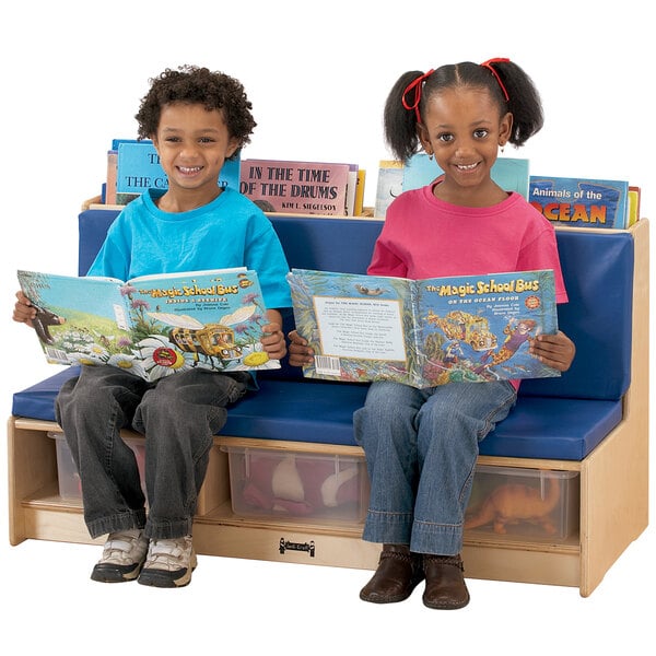 Children sitting on a Jonti-Craft wood bench with blue padded seating reading books.