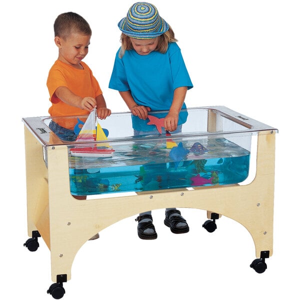 A boy and girl playing with a toy boat in a Jonti-Craft mobile sensory table filled with water.