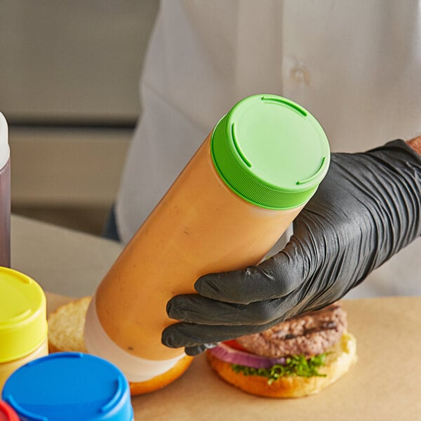 A person in gloves holding a Tablecraft light green squeeze bottle of sauce.