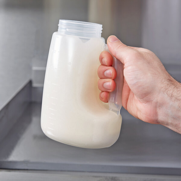 A hand holding a plastic bottle of liquid.