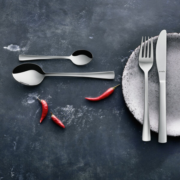 An Amefa stainless steel demitasse spoon on a plate with a fork and knife.