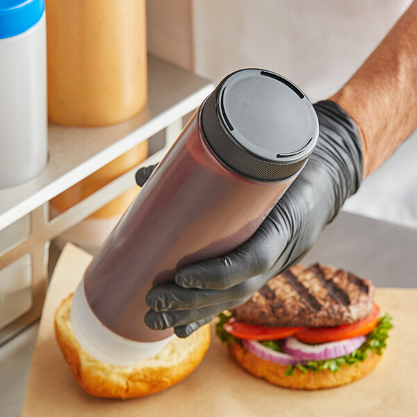 A person in gloves holding a Tablecraft black end cap on a bottle of sauce.