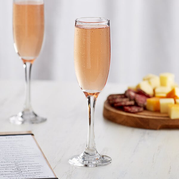 An Acopa tall flute glass of champagne next to a plate of cheese on a table.