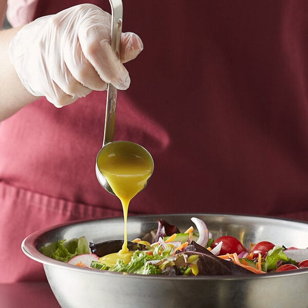 A person using a Vollrath stainless steel ladle to pour dressing onto a salad.