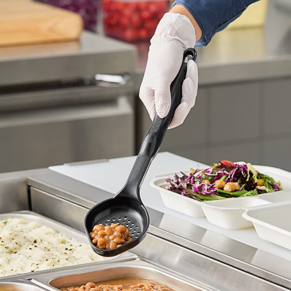 A person in gloves using a black Vollrath Spoodle to serve beans.