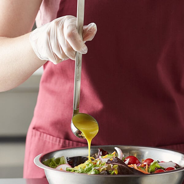 A person using a Vollrath stainless steel ladle to pour dressing on a salad.