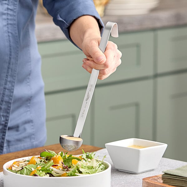A person using a Vollrath stainless steel ladle to serve salad