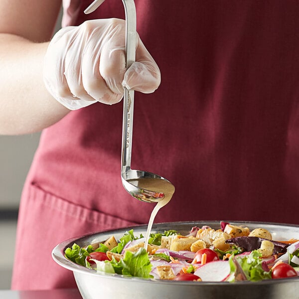 A person using a Vollrath stainless steel ladle to pour sauce over a bowl of salad.