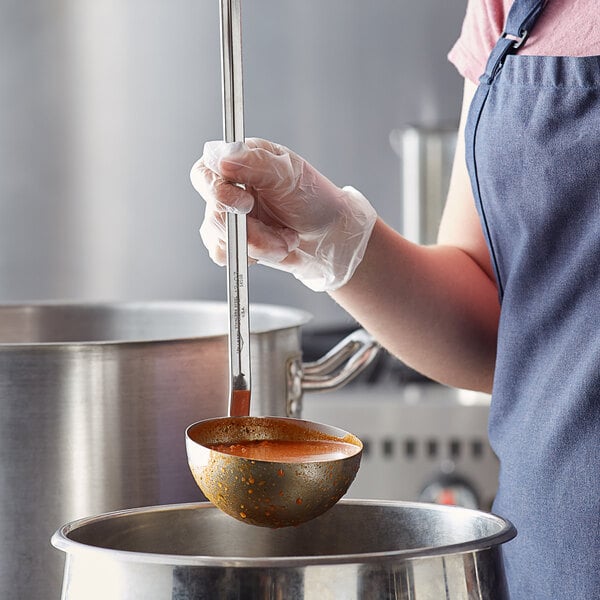 A person using a Vollrath stainless steel ladle to serve orange soup from a pot.