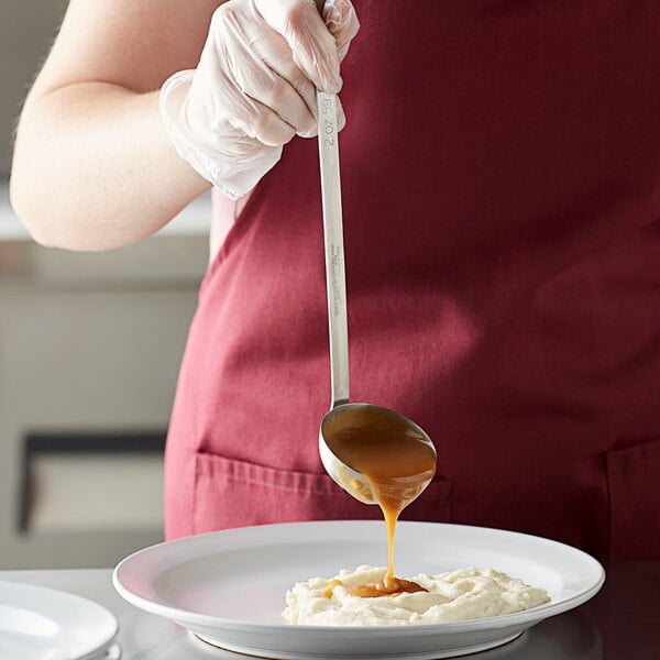 A person using a Vollrath stainless steel ladle to pour brown liquid onto a plate of food.