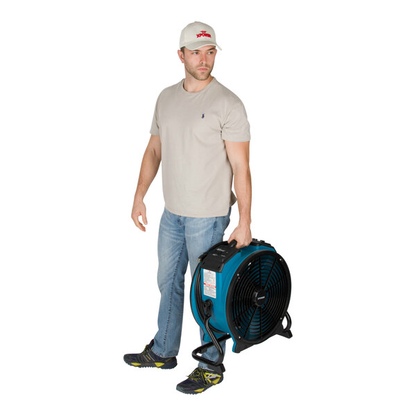 A man holding an XPOWER X-47ATR industrial fan with blue and black accents.