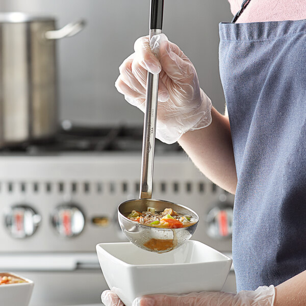 A woman using a Vollrath Two-Piece Stainless Steel Ladle to pour soup into a bowl.