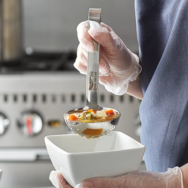 A person using a Vollrath stainless steel ladle to pour soup.