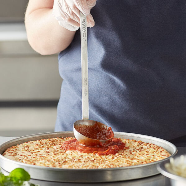 A stainless steel Vollrath ladle with red sauce in it over a plate of food.