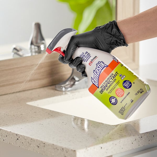 A person wearing black gloves using a SC Johnson fantastik spray bottle to disinfect a sink.