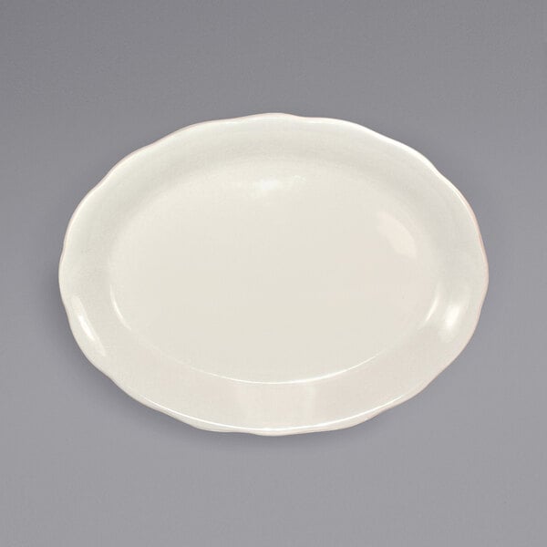 An International Tableware ivory stoneware platter with a scalloped edge on a gray surface.